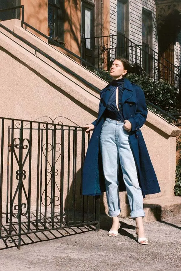 style blogger gabrielle arruda wearing same jeans and orseund iris blouse with navy trench coat to show how much a layering piece or outerwear can impact looking polished and put-together