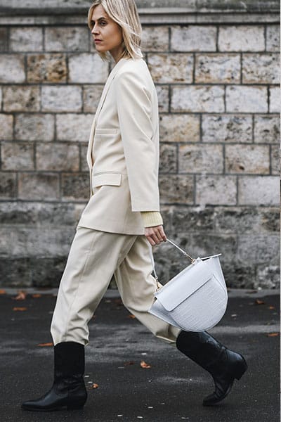  Influenceuse de STYLE vêtue d'un costume blanc avec un pantalon rentré dans des bottes avec un sac de créateur - améliorez votre style en utilisant des services de location de mode 