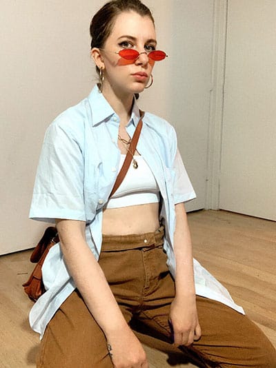 gabrielle arruda with mens pants and mens short sleeve shirt with red colored sunglasses and leather crosbody bag