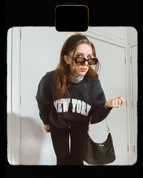 flare leggings outfit on gabrielle arruda with elastic headband, nylon prada bag, and rectangular sunglasses and "new york" sweatshirt from winter capsule wardrobe