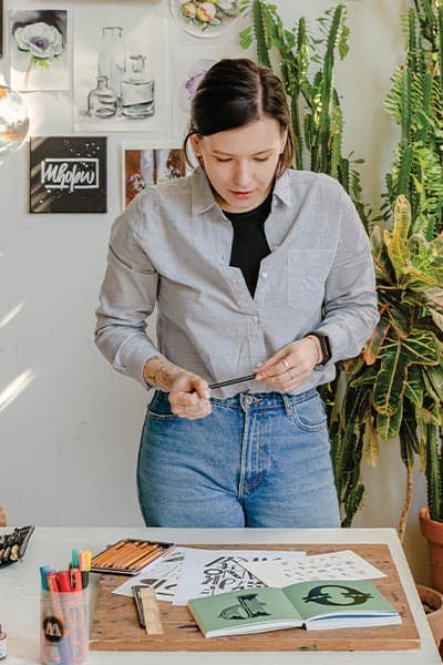 female artist in casual artsy outfit. loose jeans, black tee and light gray blouse layered over it working on drawings