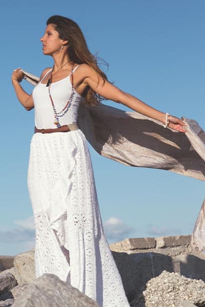 boho fashion style; woman in flowy white dress with natural bead necklace and woven belt