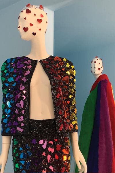 camp fashion style example, from met gala. rainbow heart piattes on black cape and skirt, rainbow furry cape in background