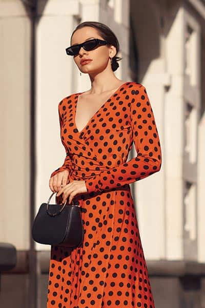 classic fashion style picture; girl in simple polka dot wrap dress with classic handbag and sunglasses and hair in bun