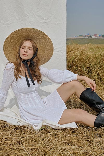 cottagecore fashion style, types of fashion styles with pictures.  girl with broad straw hat, white puff sleeve cotton dress and black boots on 