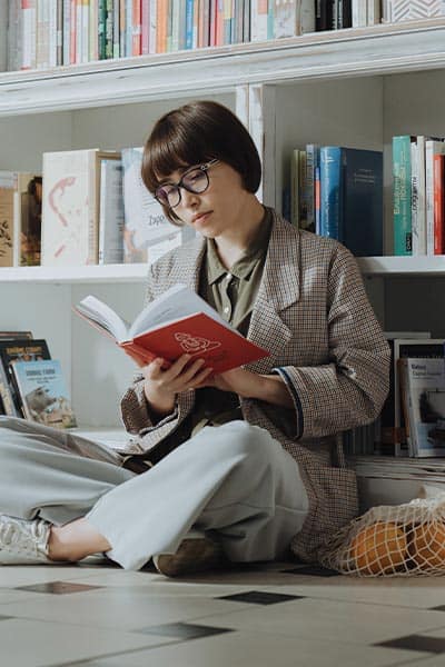 geeky chic fashion style, girl reading book with glasses and loose shirt and trousers with classic sneakers