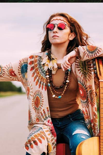 hippie fashion girl, girl with round sunglasses, 70's style print blouse, feathers in hair, and jeans