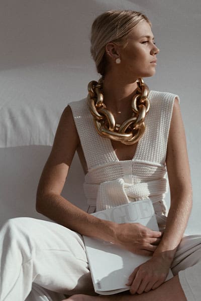 spring fashion trends 2021, elevated crochet and knits. woman in tie front crochet top with x-large gold chain and vogue magazine in her hand