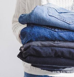 woman holding a stack of jeans, improve style by knowing what you have in your closet