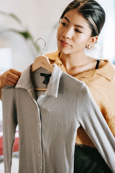 woman trying a shirt on by holding it up to her, fashion mistake- buying the same size in clothes no matter the style or brand