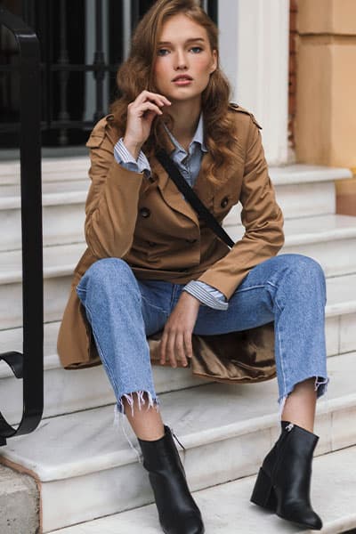 how to look polished, look at the entire outfit and style. woman in trench coat with jeans, and blouse and black ankle boots with loose waves in hair and done makeup