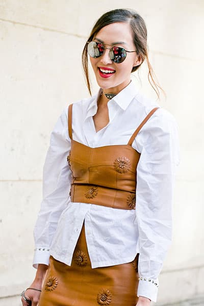 style influencer wearing white blouse with leather crop top and skirt. leather crop top layered over white blouse 