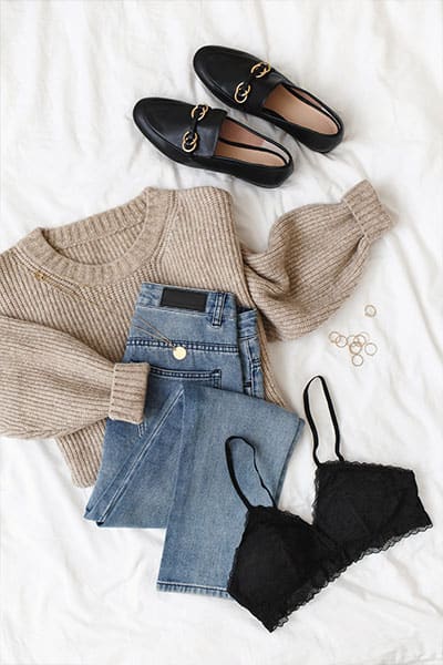 flat lay of outfit with loafers, sweater, jeans, and black bra