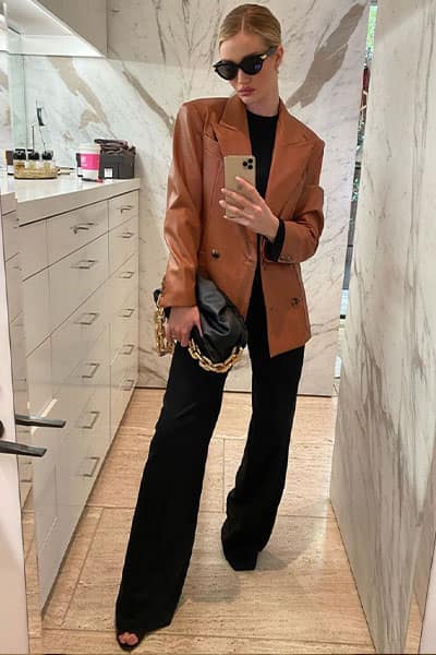 rosie huntington-whiteley mirror selfie wearing black tee with wide leg black pants, heels, bottega pouch, and cognac leather blazer with black sunglasses