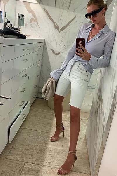 rosie huntington whitley style: rosie wearing fitted blouse with white bermuda denim shorts, clear heels, and bottega venetta pouch bag 