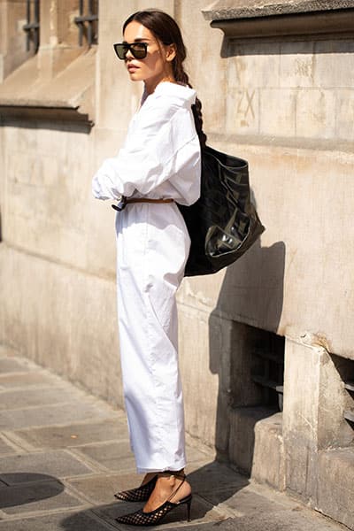  frau in Paris trägt weißen Button-up mit weißen Hosen und schwarze Sonnenbrille verkörpert Französisch Mädchen Stil 