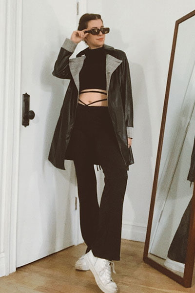 gabrielle arruda wearing black flared leggings with tie detail, and leather trench coat with white sneakers and black crop top 