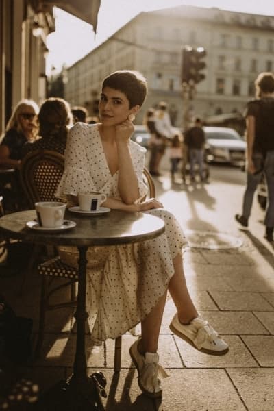 french girl in cafe wearing classic sneakers and a neutral print wrap dress