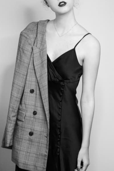 woman wearing black slip dress with buttons on side and blazer draped over shoulder