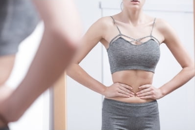 image of woman looking in mirror and grabbing her stomach/sucking in to show you need to separate body hang ups from your style
