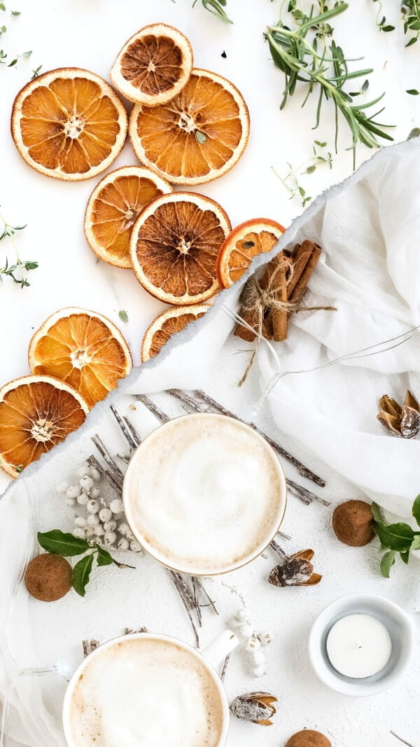 two images diagonally cut, top image of dried oranges with green plants around, and bottom image of hot cocoa and white berries and twigs.  Light-colored backgrounds, bright images.  holiday wallpaper background