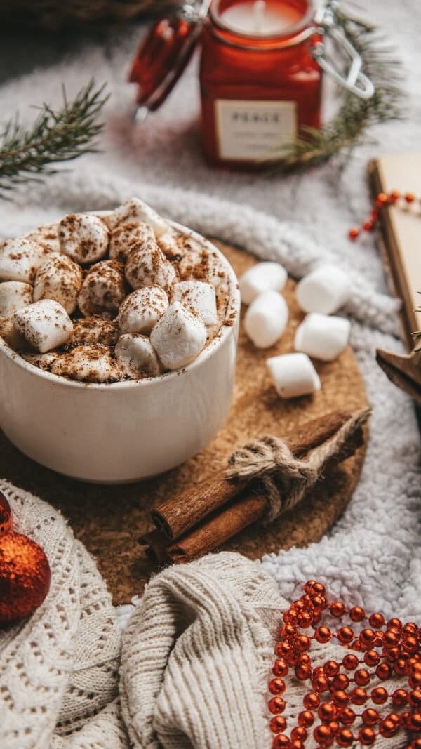 holiday table with a focus on a white mug of hot coco with marshmellows. 