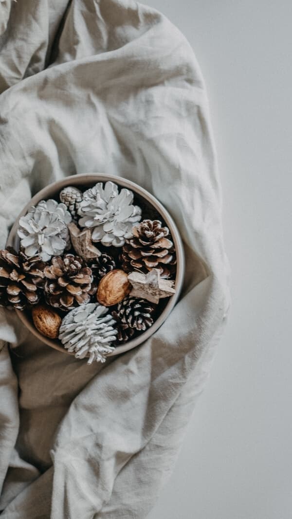 white linen blanket with bowl of pinecones, natural elements, minimalist holiday wallpaper for iphone