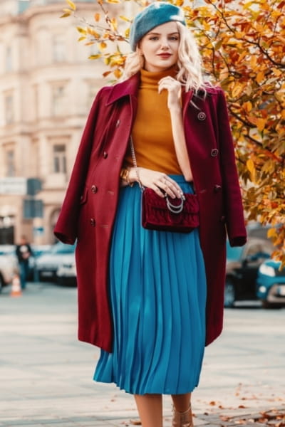 woman with rectangle body shape adding curve to her figure by wearing a turtleneck with a longer coat draped over and a bright soft-pleated skirt 