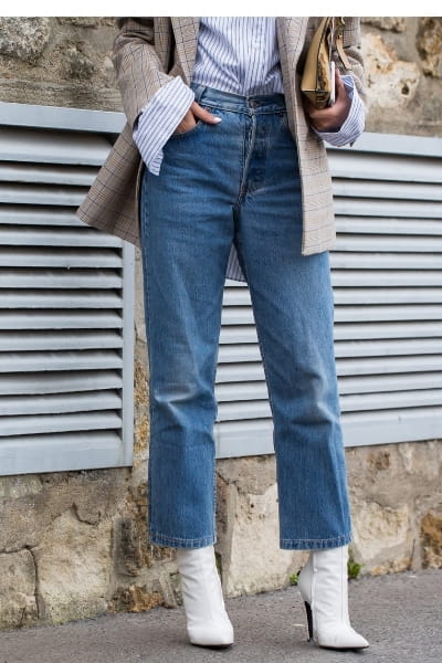 woman with blazer and shirt (french-tucked) into a pair of straight leg jeans and pointed white boots 
