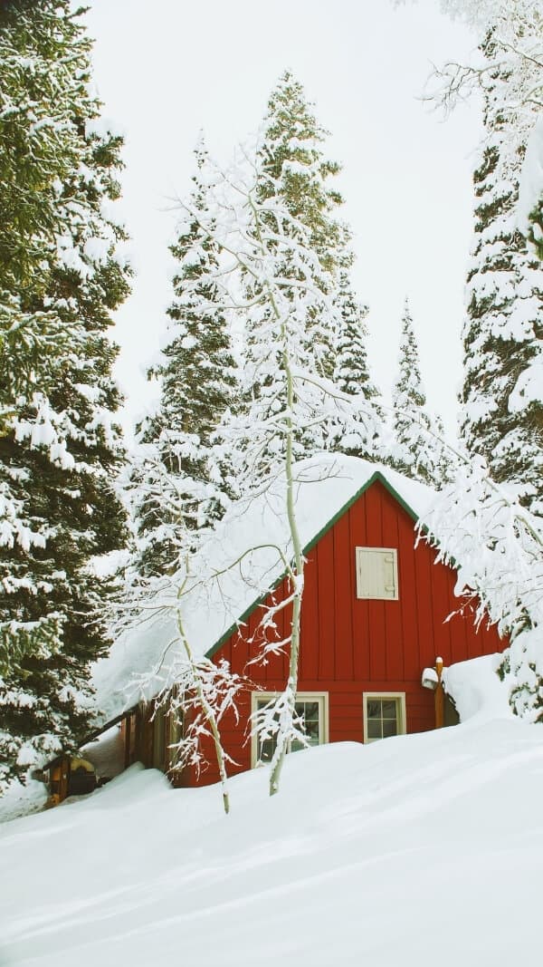 red cottage on snowy hill, on-mountain with forest behind it. december wallpaper for iphone