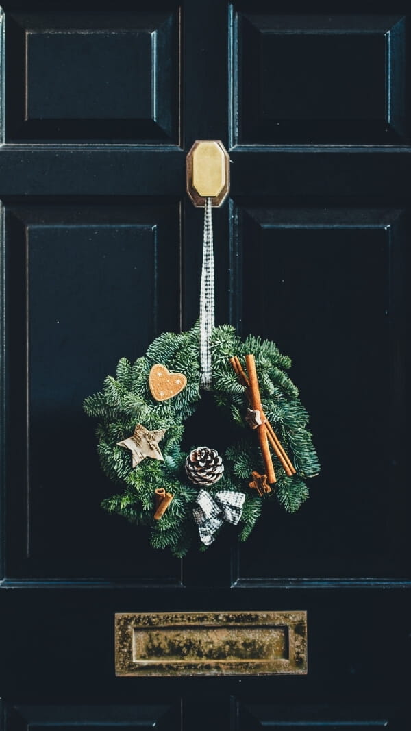 black door with holiday wreath hanging, wreath has cinnamon, star, pinecone decorations. simple christmas wallpaper background for iphone 