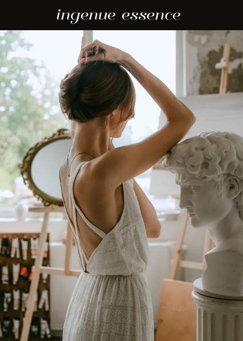 woman holding up her hair wearing a light and airy white dress to show ingenue style essence