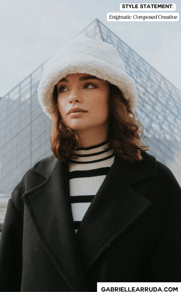style statement example "marie": chic french girl in black coat with striped turtleneck and fuzzy bucket hat in front of the Louvre